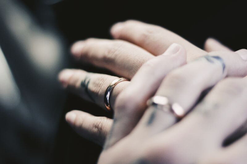 Close up of two people holding hands, with their wedding rings showing