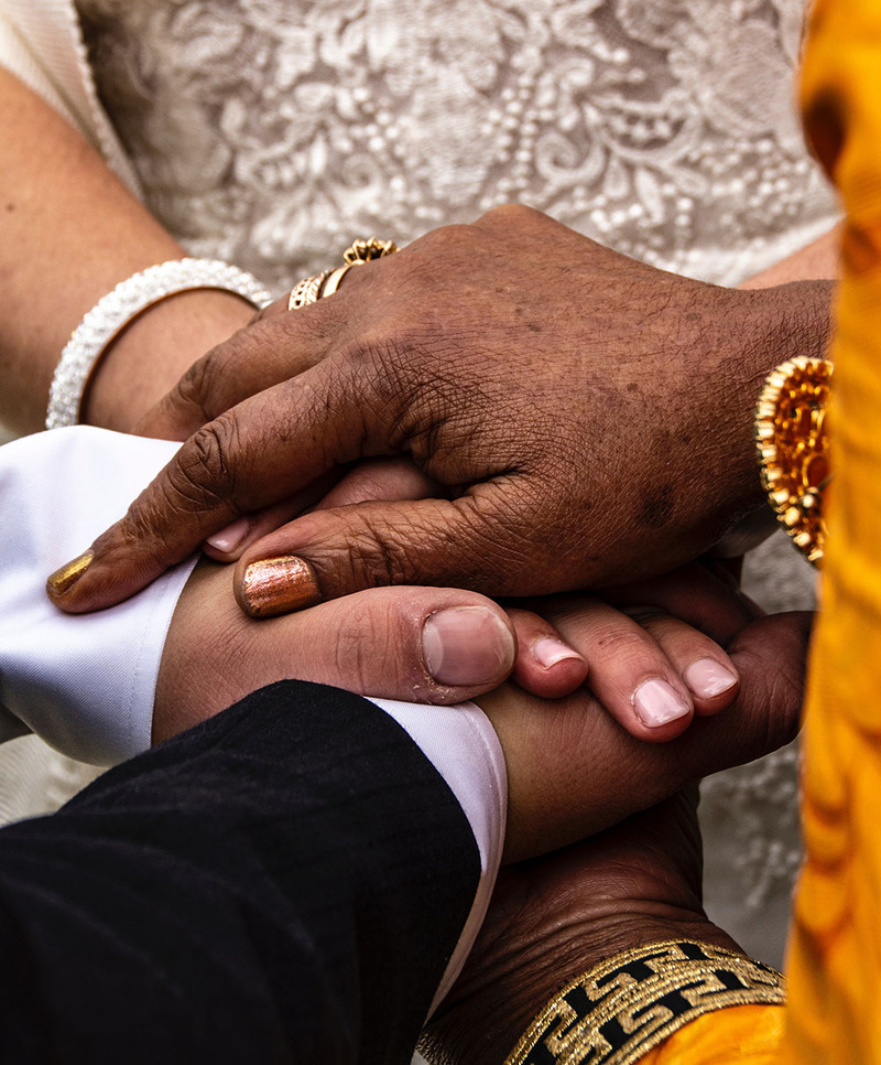 Close up photo shows a minister resting her hands on the hands of two newlyweds during a wedding ceremony 