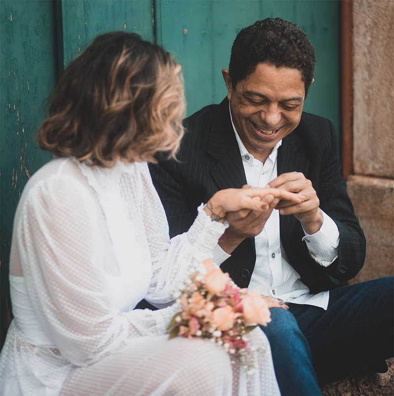 Newlyweds sit together on the steps beside a blue door, the groom admires the bride's ring 