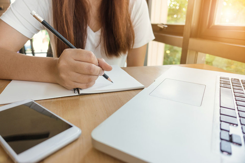 Close up photo of a young woman holding a pencil and writing notes while planning her wedding ceremony