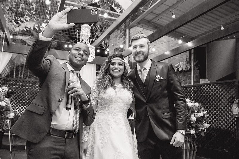 Wedding officiant holds up a phone to take a selfie of himself and two newlyweds he just married