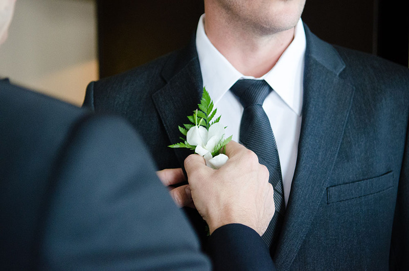 Close up as two grooms prepare for a wedding ceremony, a groom places a flower on the other's jacket