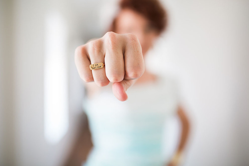 A bride holds out her hand, in a fist, to show off a gold ring that has the phrase "I am a badass" etched into its surface