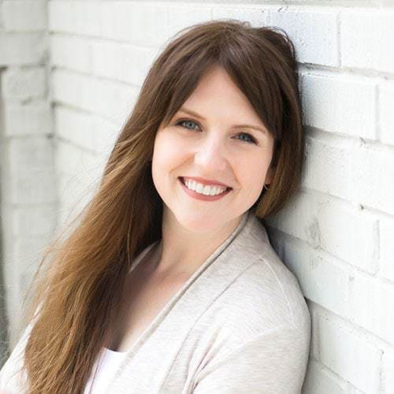 Laura C. Cannon smiles at the camera while leaning against a wall outdoors in the sunshine