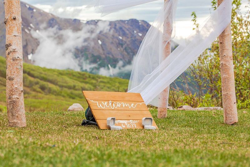 Photo of a wedding welcome sign propped up outside in front of a beautiful mountain on the horizon