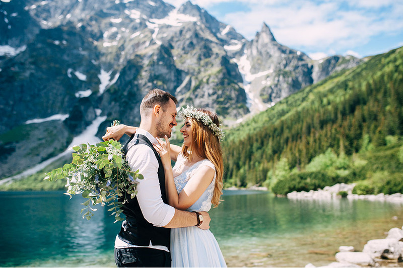Bride and groom embrace in front of a snowy mountain outdoors after their wedding ceremony, smiling and happy