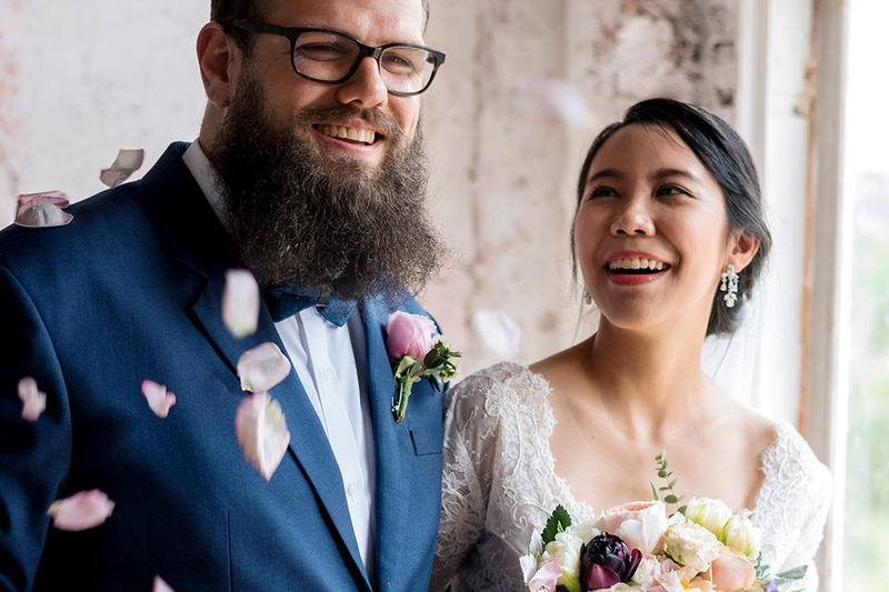 Close up of two newlyweds smiling on their wedding day, with rose petals falling on their shoulders