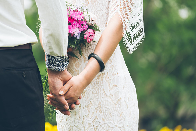 Close up photo of a South Carolina bride and groom holding hands on the wedding day outdoors, the bride carries a bouquet of pink and white flowers