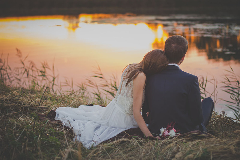 Newlyweds sit next to a lake at sunset