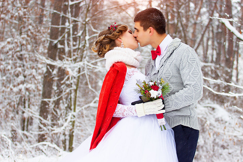 Newlyweds kiss during a wedding ceremony outdoors in the snowy woods