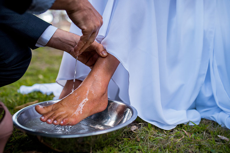 Close up of a groom sprinkling water on a bride's feet during a Christian feet washing wedding ceremony