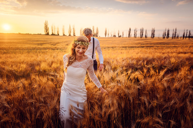 Newlyweds hold hands in a field lit by golden light at sunset