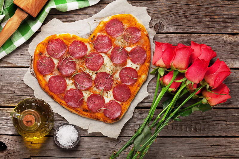 A heart shaped pizza with cheese and pepperoni on a table with roses