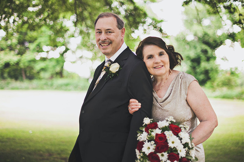 An older couple link arms to pose for a photo outdoors following their renewal of vows ceremony