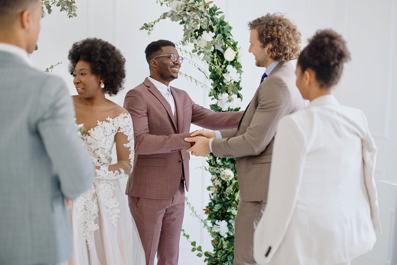 Ceremonia de boda en el interior, los novios recién casados ​​saludan a amigos y familiares en celebración después de casarse, el oficiante observa con una sonrisa