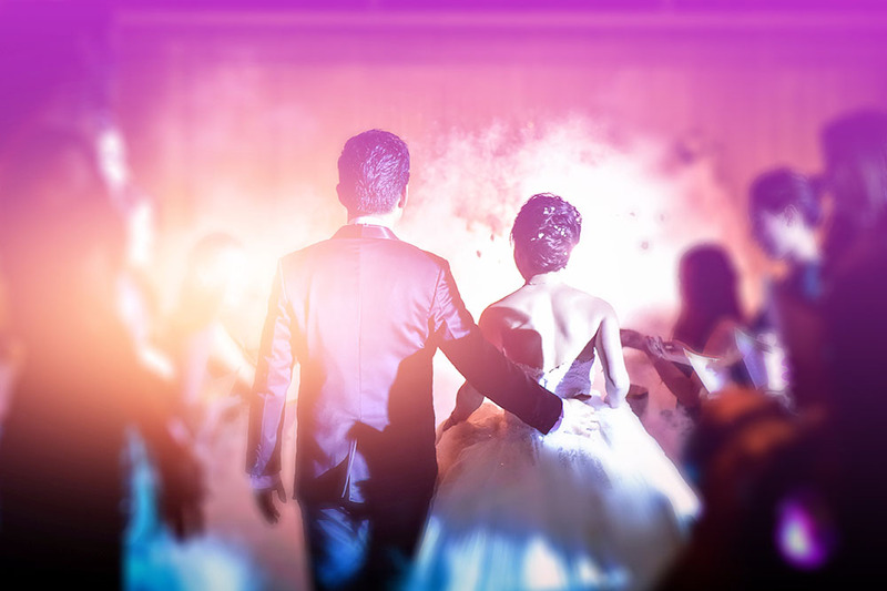 Newlyweds walk down the aisle in a room with pinkish purple light