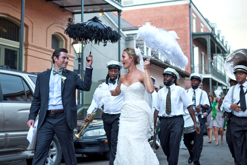 Newlyweds walk down the street in New Orleans accompanied by a jazz marching band on their wedding day