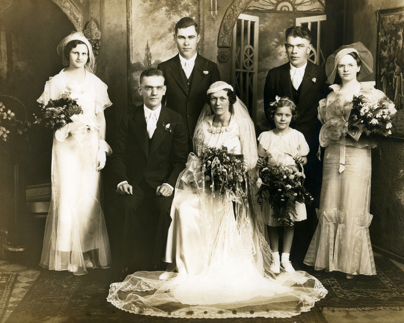 Black and white vintage wedding photo with the bride and groom, bridesmaids and groomsmen, all wearing formal attire. 