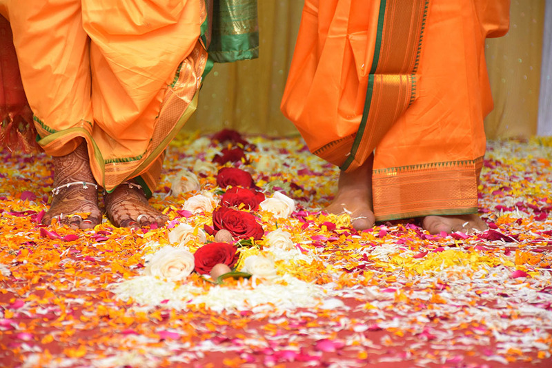 close up shows a bride and groom standing barefoot on a path decorated with flowers and petals for the Saptapadi ceremony on their wedding day