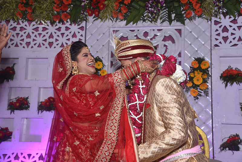 A bride laughs as she places the red and white garland around the groom's neck during the Varmala Indian wedding tradition