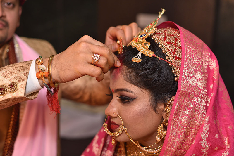 Close up shows an Indian groom placing sindoor on the bride's hair parting during the wedding ceremony