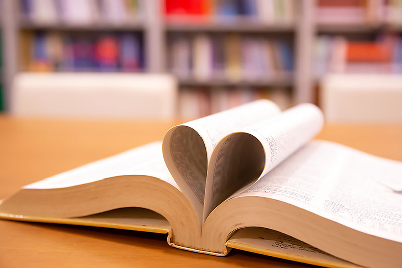 A book rests on the table, open, with its pages curved inward in the shape of a heart