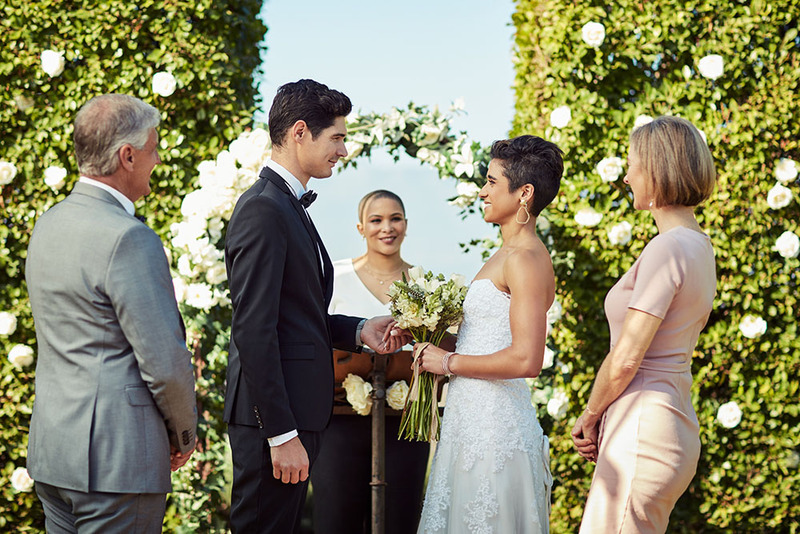 A groom and bride stand with their parents and the wedding officiant in front of the marriage arch. 