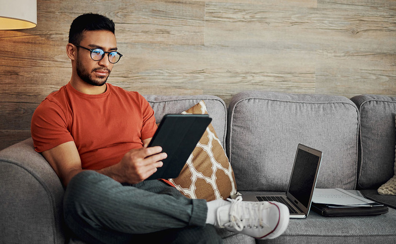 A young man fills out the AMM Minister ordination form on his tablet while sitting comfortably on the couch at home