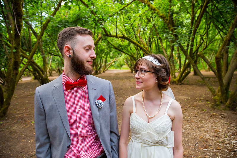 A young bride and groom pose in the forest on their wedding day, they look quirky and cute and nontraditional