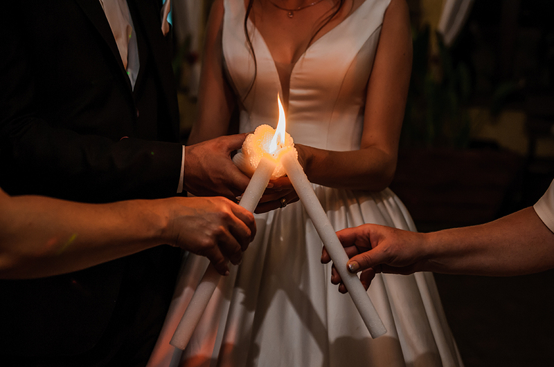 Close up shows four people participating in a unity candle ceremony