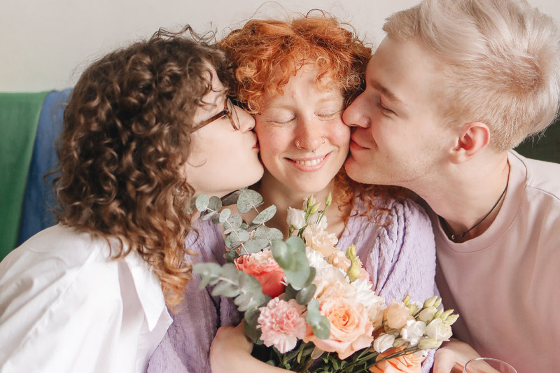 Two partners kiss a third partners cheeks in a cute poly relationship photo