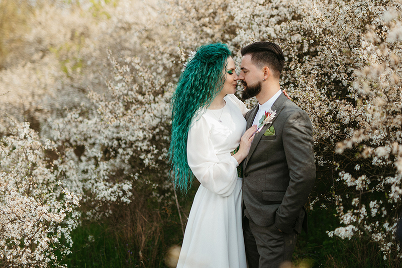 Bride and groom pose in the spring outdoor wedding, behind them are trees with white blossoms