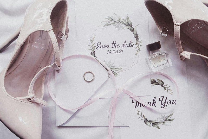 Stylized photo shows pinkish white wedding heels next to wedding save the dates , a wedding ring, and other decor