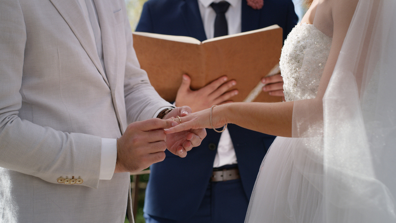 A wedding officiant reads from a script to the bride and groom, close up photo