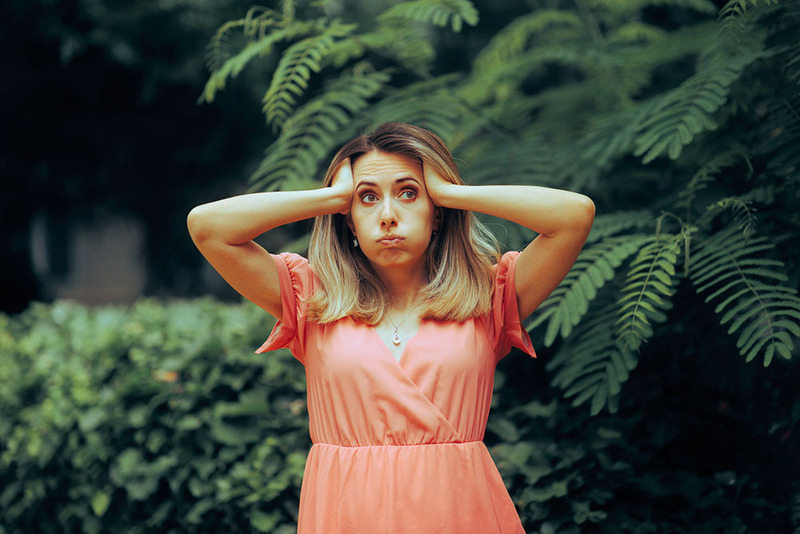A woman in a coral colored dress holds her ands up to her head in exasperation during an outdoor wedding