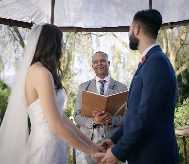 Wedding officiant smiles at a bride and groom during an outdoor wedding ceremony