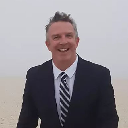 Photo of wedding officiant Christopher Shelley, wearing a suit and tie and smiling at the camera