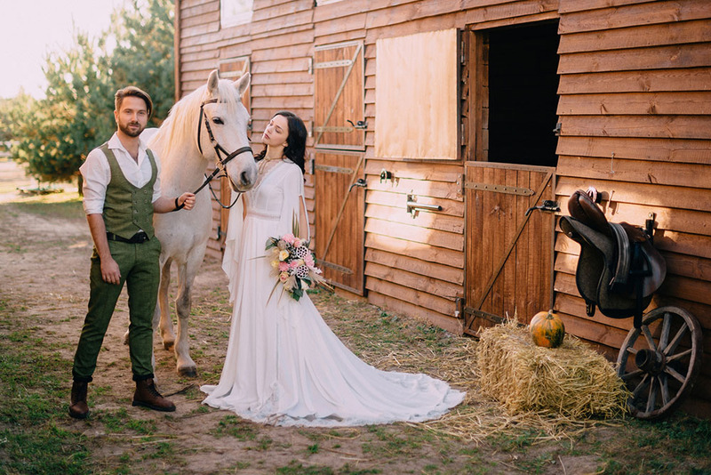 Bride and groom standing with a horse outside a barn on the wedding day