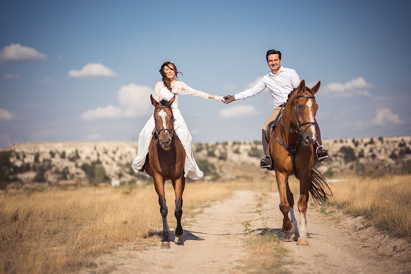 Bride and groom, newlyweds riding horses together outside in a sunny field