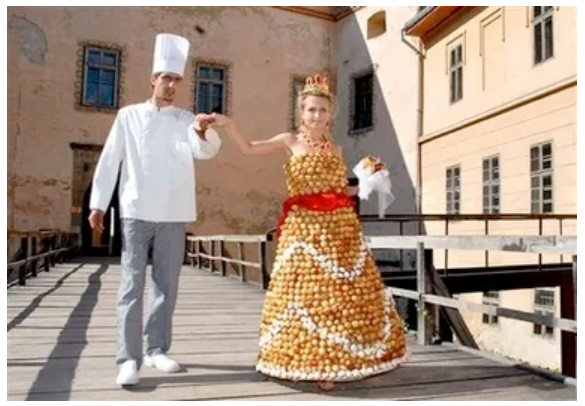 The baker walks with his bride, holding her hands, while she wears the edible wedding dress made from cream puffs