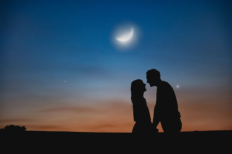 Newlyweds kiss under the night sky with a waxing crescent moon above
