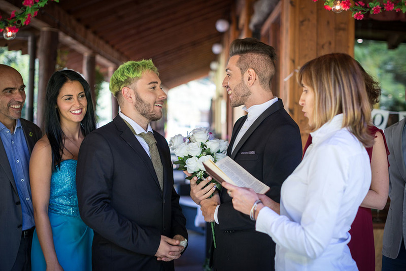 Wedding officiant performs a ceremony for two grooms while friends and family watch