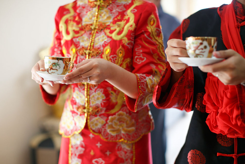 Close up of a bride and groom dressed in traditional Chinese wedding attire holding tea during the tea ceremony