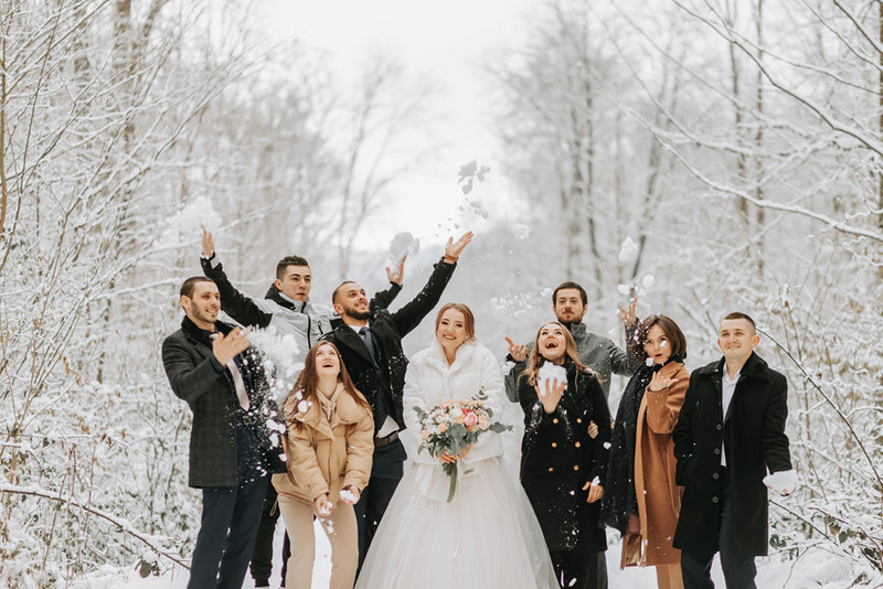 Bride and her wedding party friends play in the snow while posing for a photo during a fun winter wedding