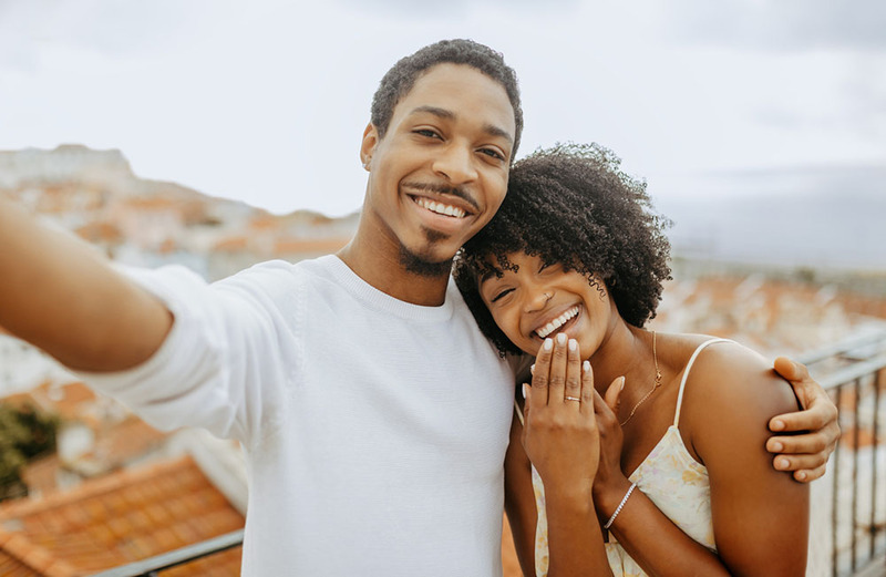 Selfie of a young couple smiling, the woman shows off her engagement ring or wedding ring, they are happy and in love! 