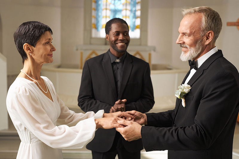 Officiant performs a wedding ceremony inside a church for bride and groom, who are holding hands and smiling 
