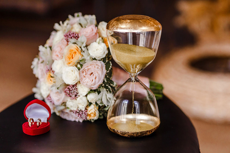 Hourglass and wedding rings on a wedding table next to flowers