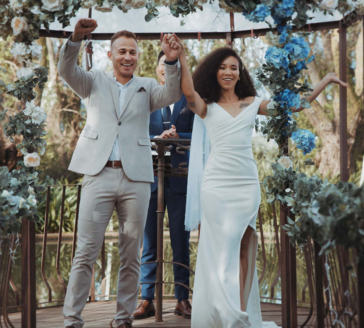 Groom and bride raise their hands in excitement after being pronounced married by the wedding officiant