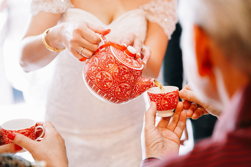 CLose up of a bride in a white wedding dress pouring tea out of decorative tea pot during the Chinese wedding tea ceremony