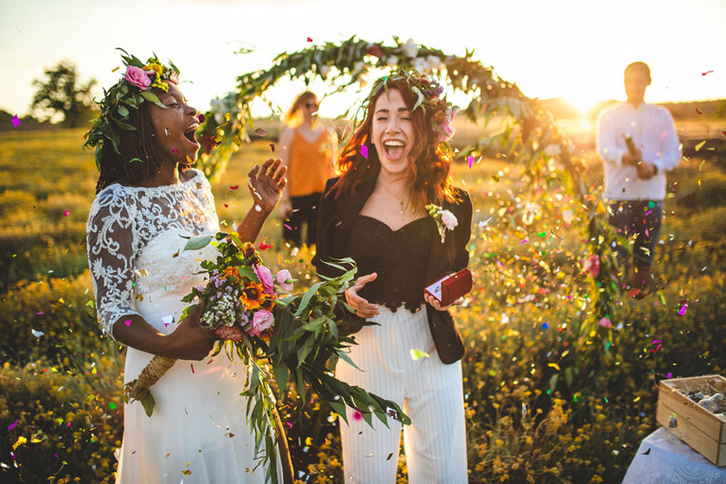 Brides eloping with friends outside in a beautiful field at sunset, they have flower wreaths on their heads and its very joyful